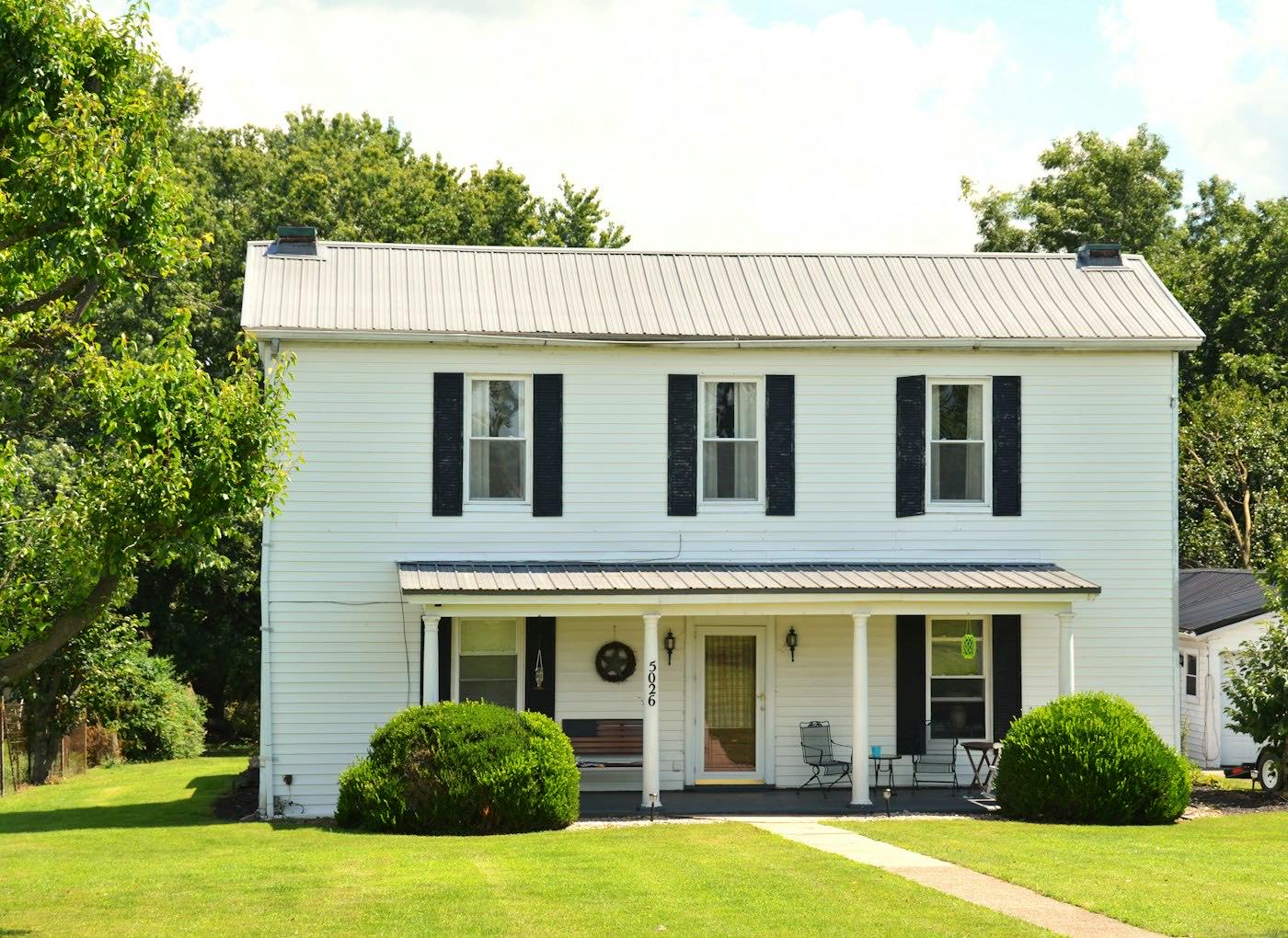 A white two-storey house with black shutters and a green front lawn