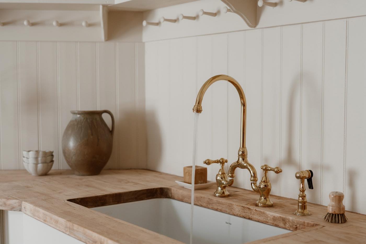 A brass tap running into a butler sink in a pale wood kitchen